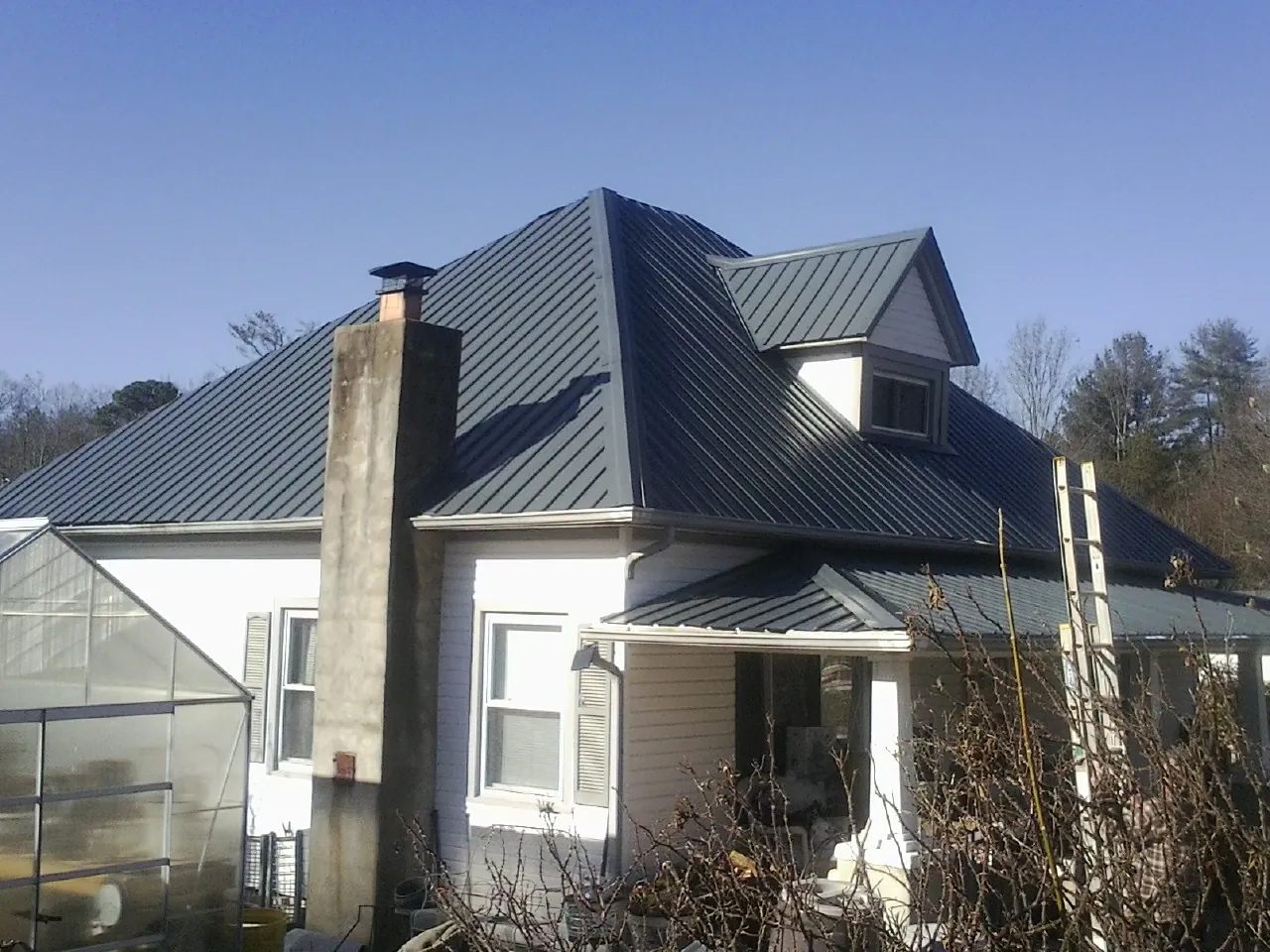 Dark blue standing seam metal roof on a white farmhouse with dormer — Slate & Tile Roof Repair by Roofing Brothers in Crouse