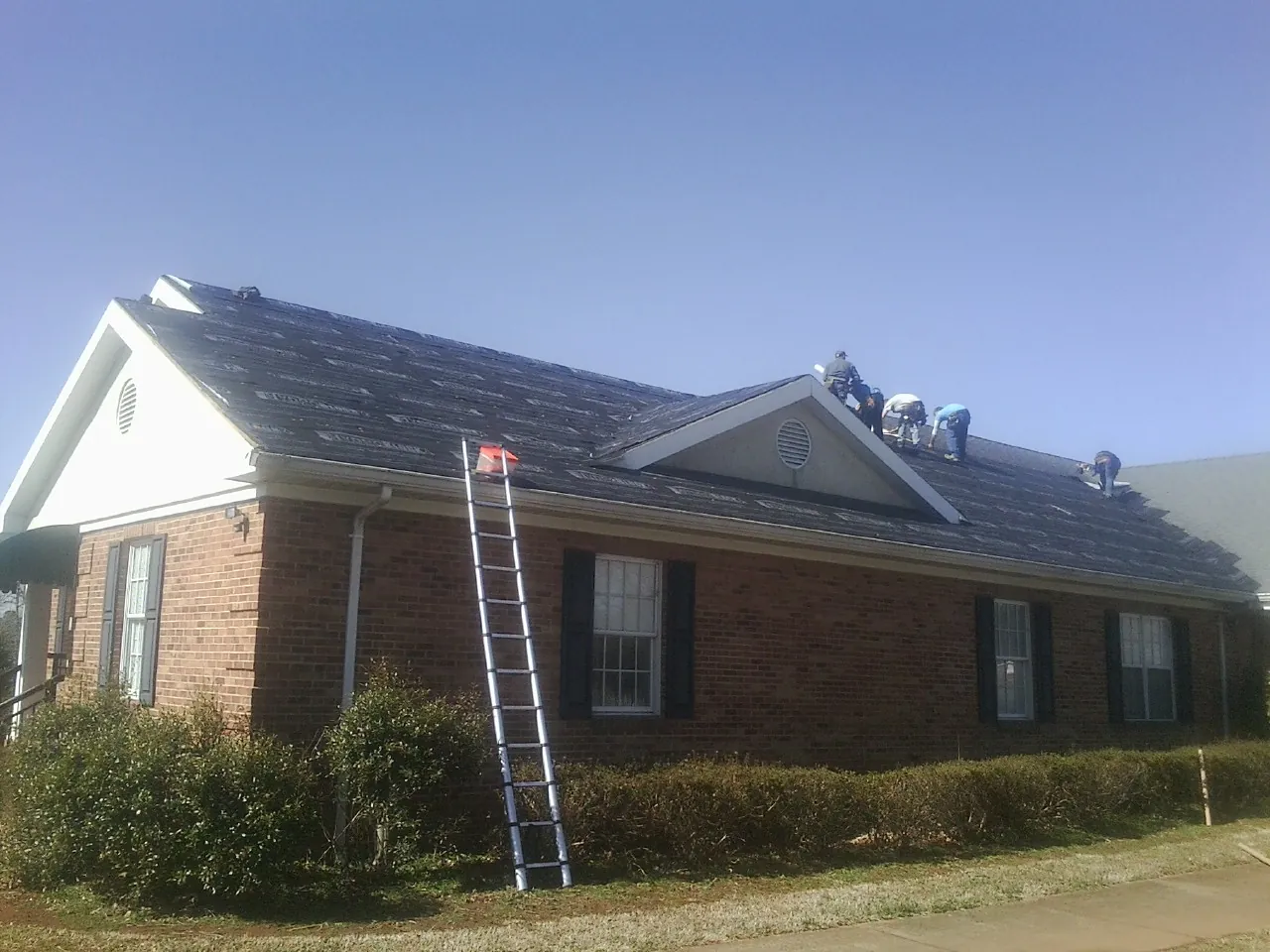 Crew tearing shingles off a brick ranch roof with a ladder set — Emergency Roof Repair work by our crew in Crouse