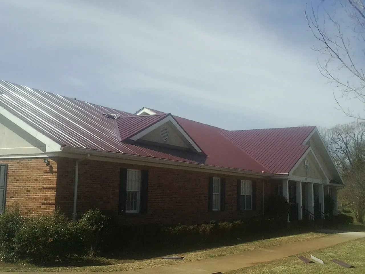 Red metal roof with gabled entries on a long brick building, from a Hail Damage Roof Repair job in Crouse