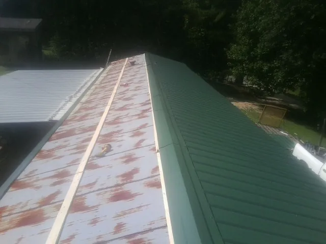Old rusted panels beside newly installed green metal roofing — Wind Damage Roof Repair by Roofing Brothers in Crouse