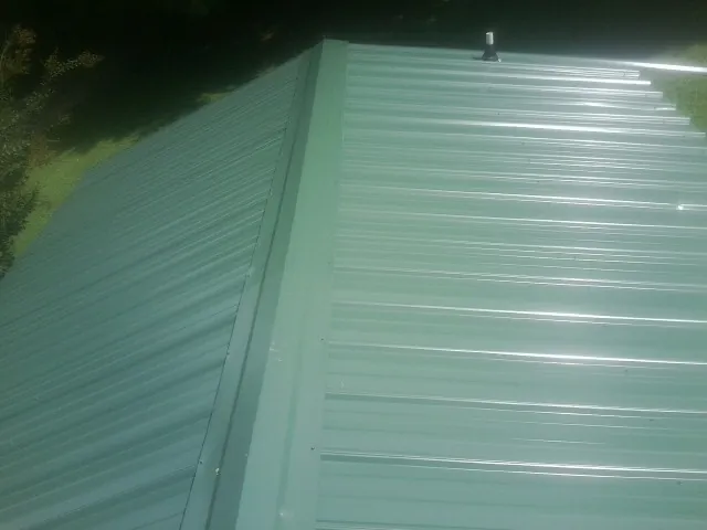 New green metal panels meeting at the ridge of a roof — Flat Roof Repair work by our crew in Crouse