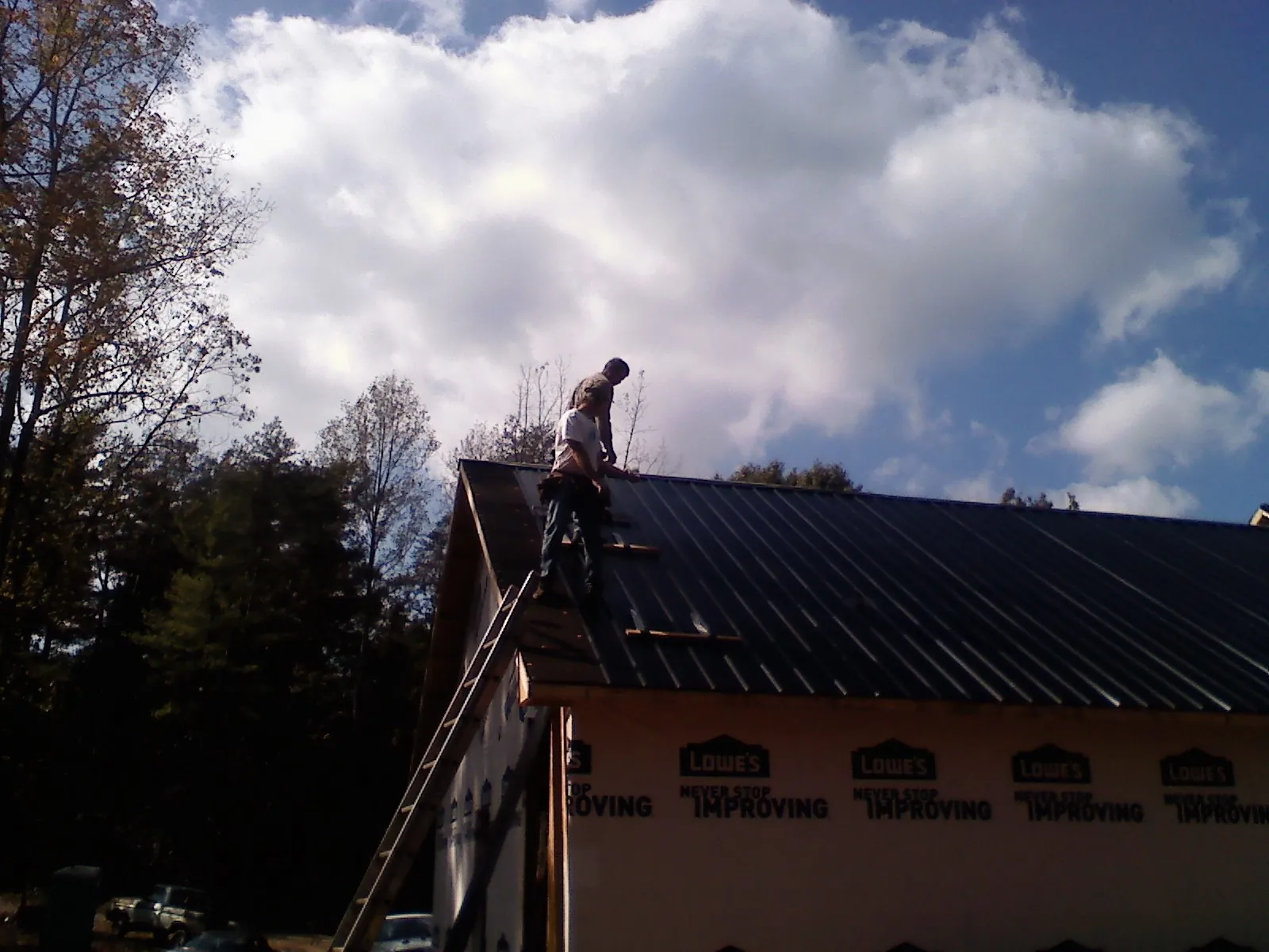Roofer fastening dark metal panels high against a cloudy sky, from a Roof Inspection job in Crouse
