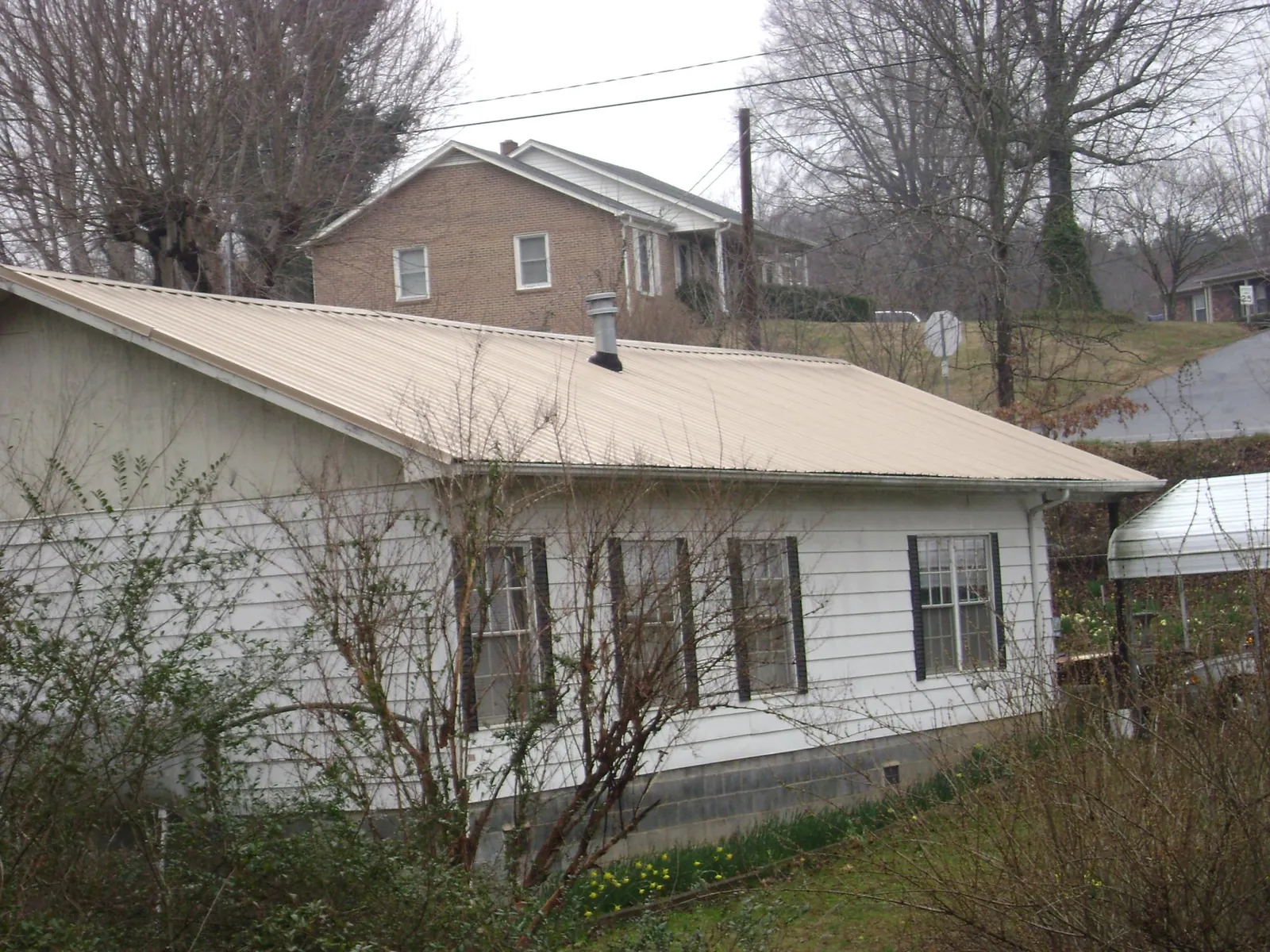 Tan metal roof on a white sided house set into a hillside — Commercial Roofing by Roofing Brothers in Crouse