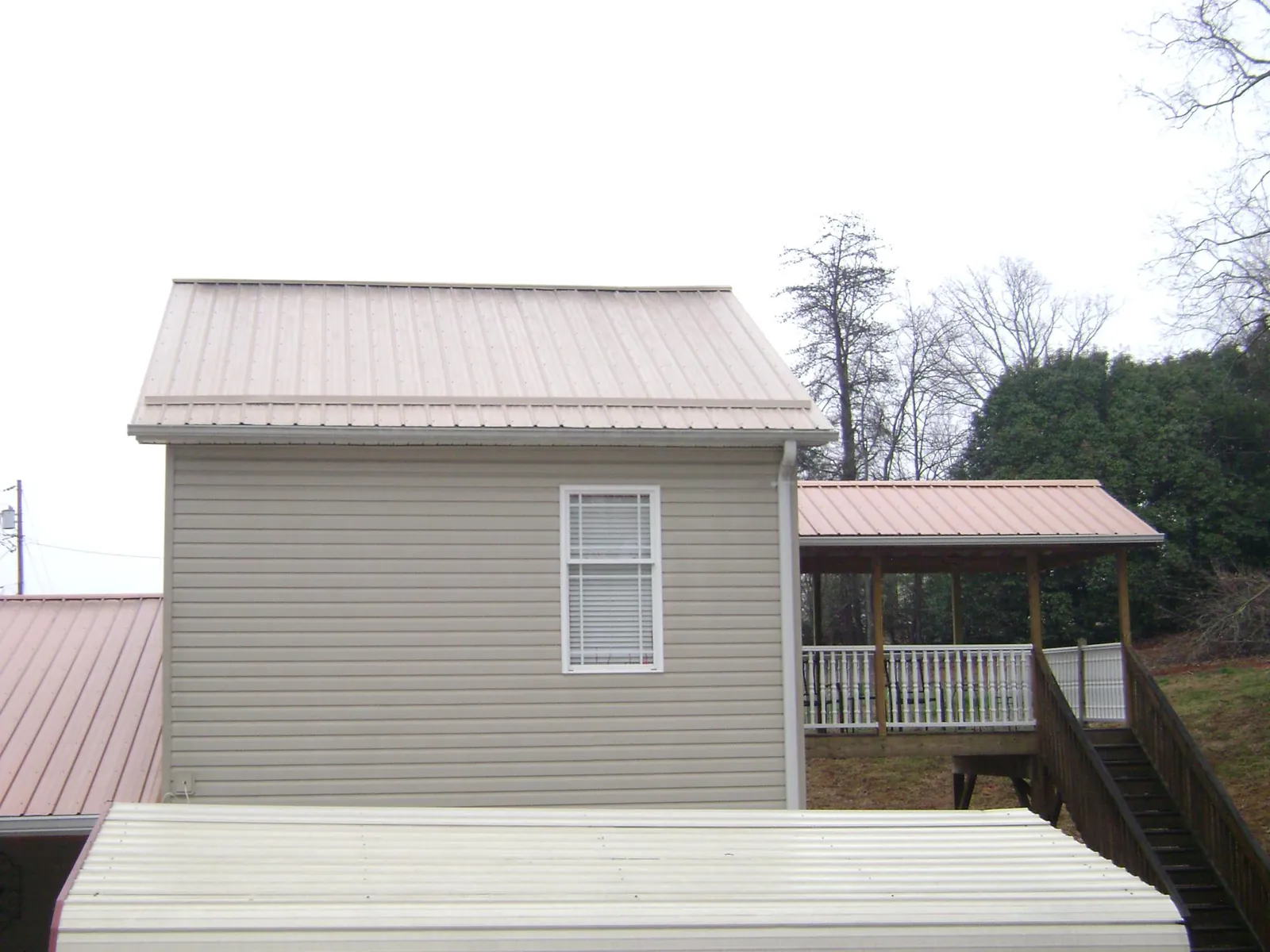Tan metal roofs on a two story addition and attached porch, from a Roof Replacement job in Crouse