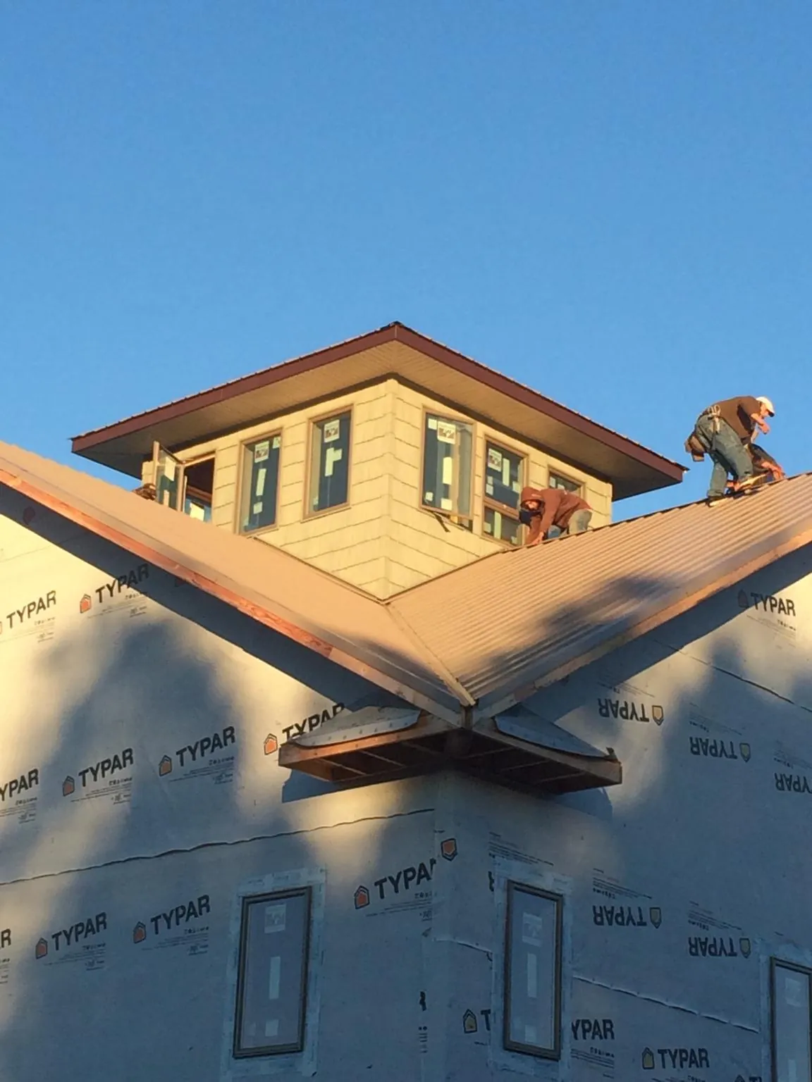 Roofers working around a rooftop cupola on a new metal roof at sunset — Roof Waterproofing in Crouse by Roofing Brothers